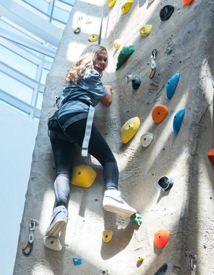 A young woman ascending a rock climbing wall.